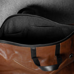 Brown leather duffel bag with black interior on a gray background