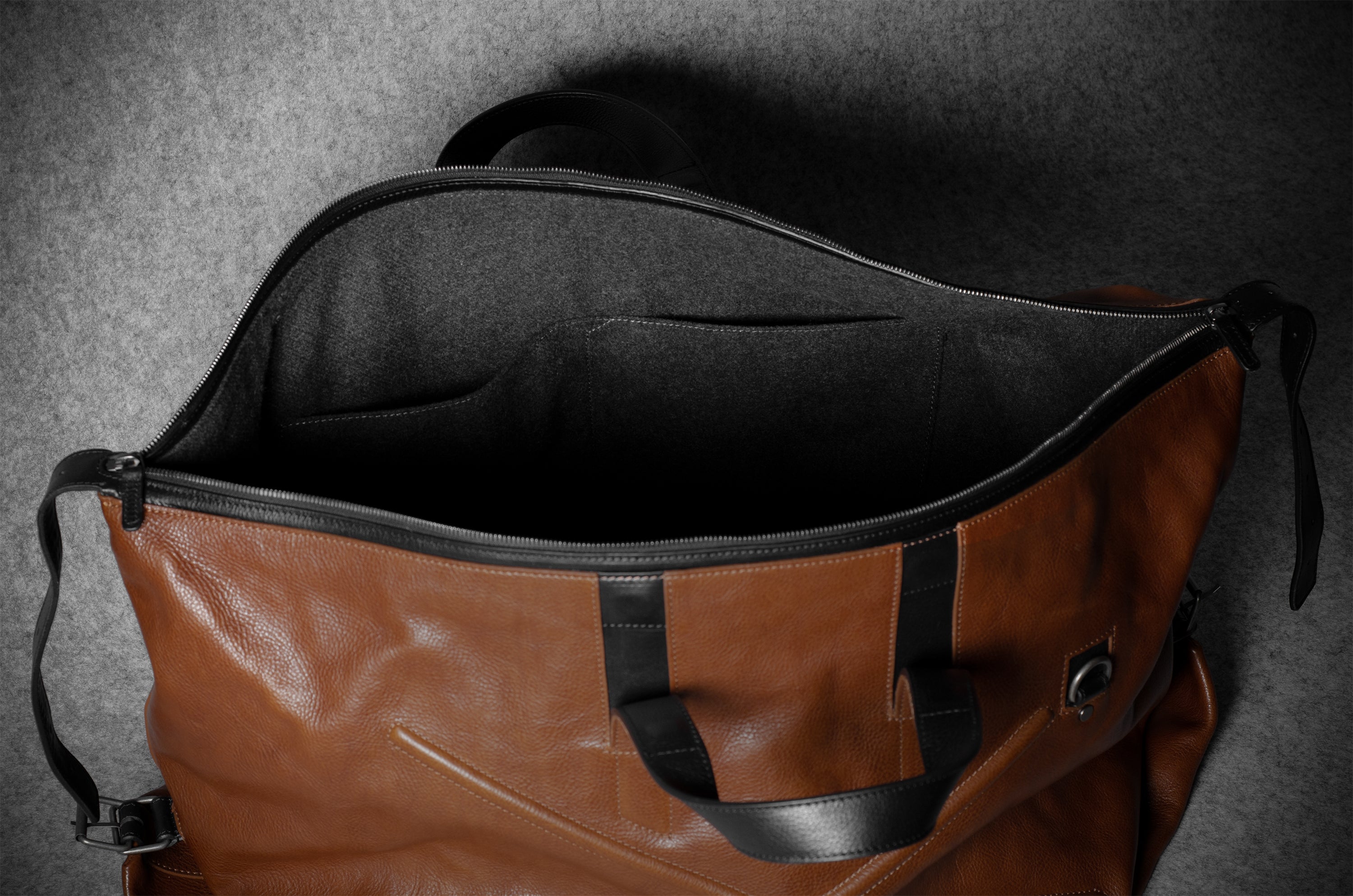 Brown leather duffel bag with black interior on a gray background