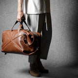 Person holding a brown leather duffel bag against a gray background