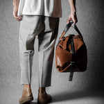 Person holding a brown leather bag against a gray background