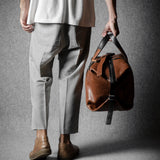 Person holding a brown leather bag against a gray background