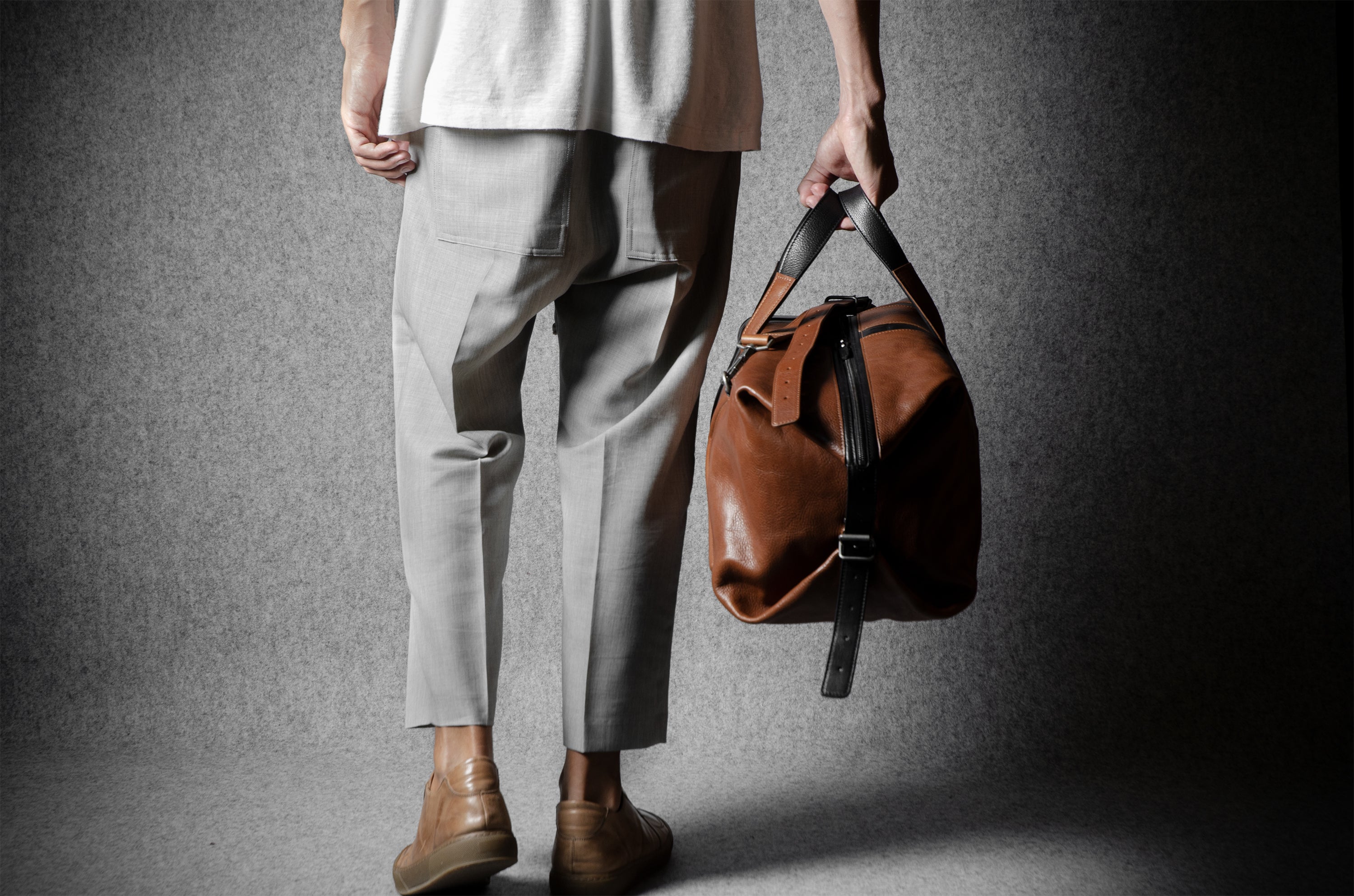 Person holding a brown leather bag against a gray background
