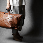 Person holding a brown leather bag against a gray background