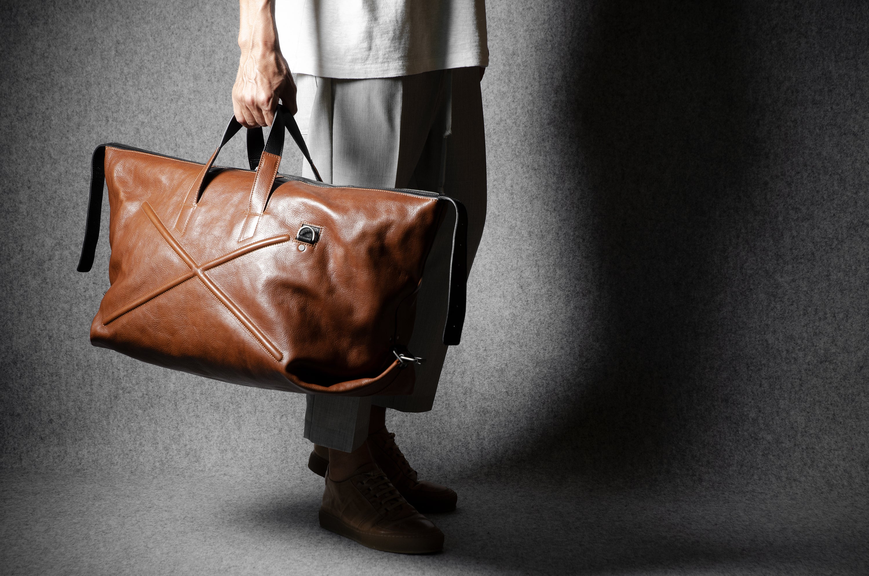 Person holding a brown leather bag against a gray background