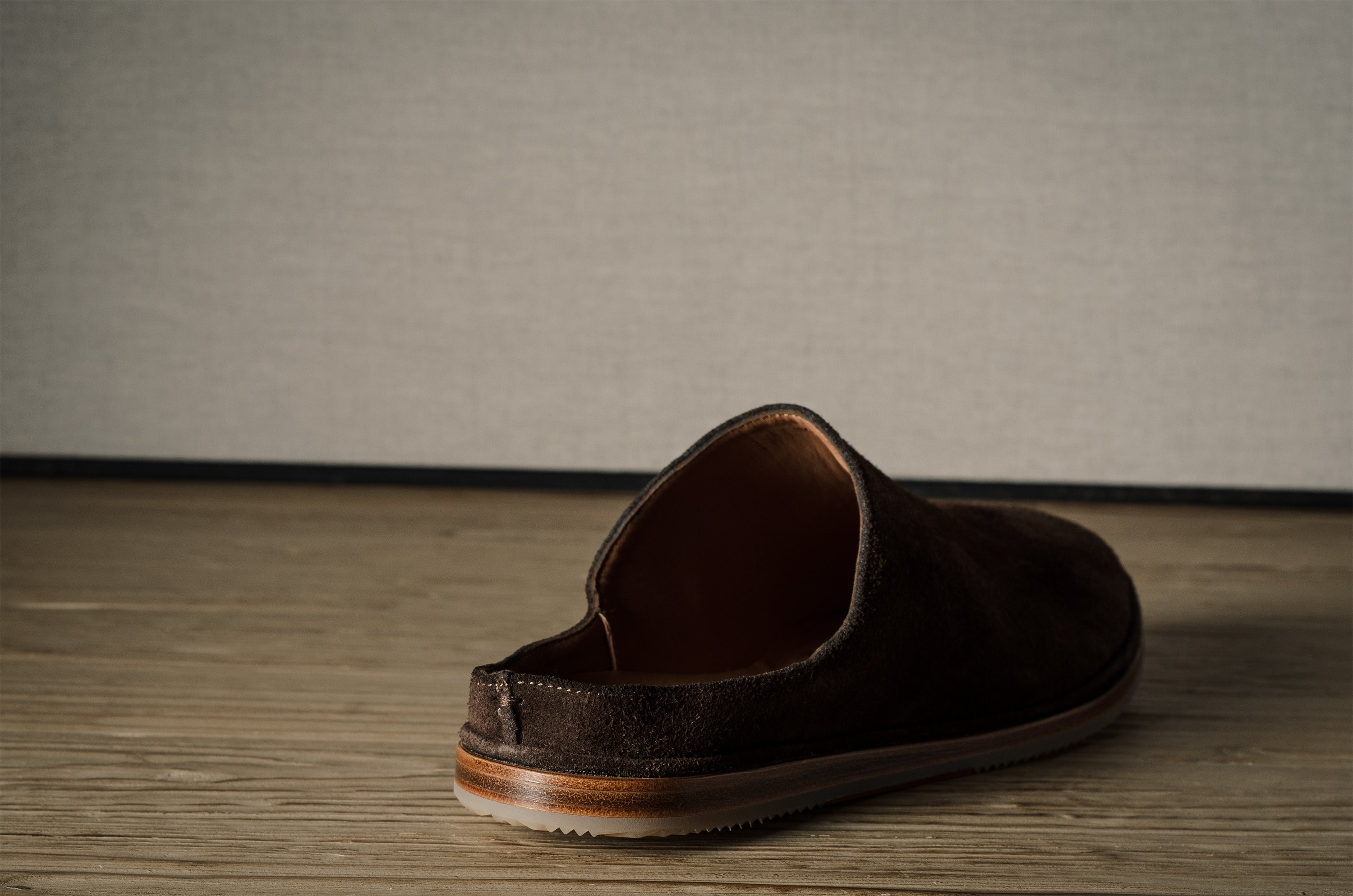 A Brown suede slipper on a wooden background.