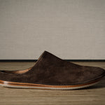 A Brown suede slipper on a wooden background.
