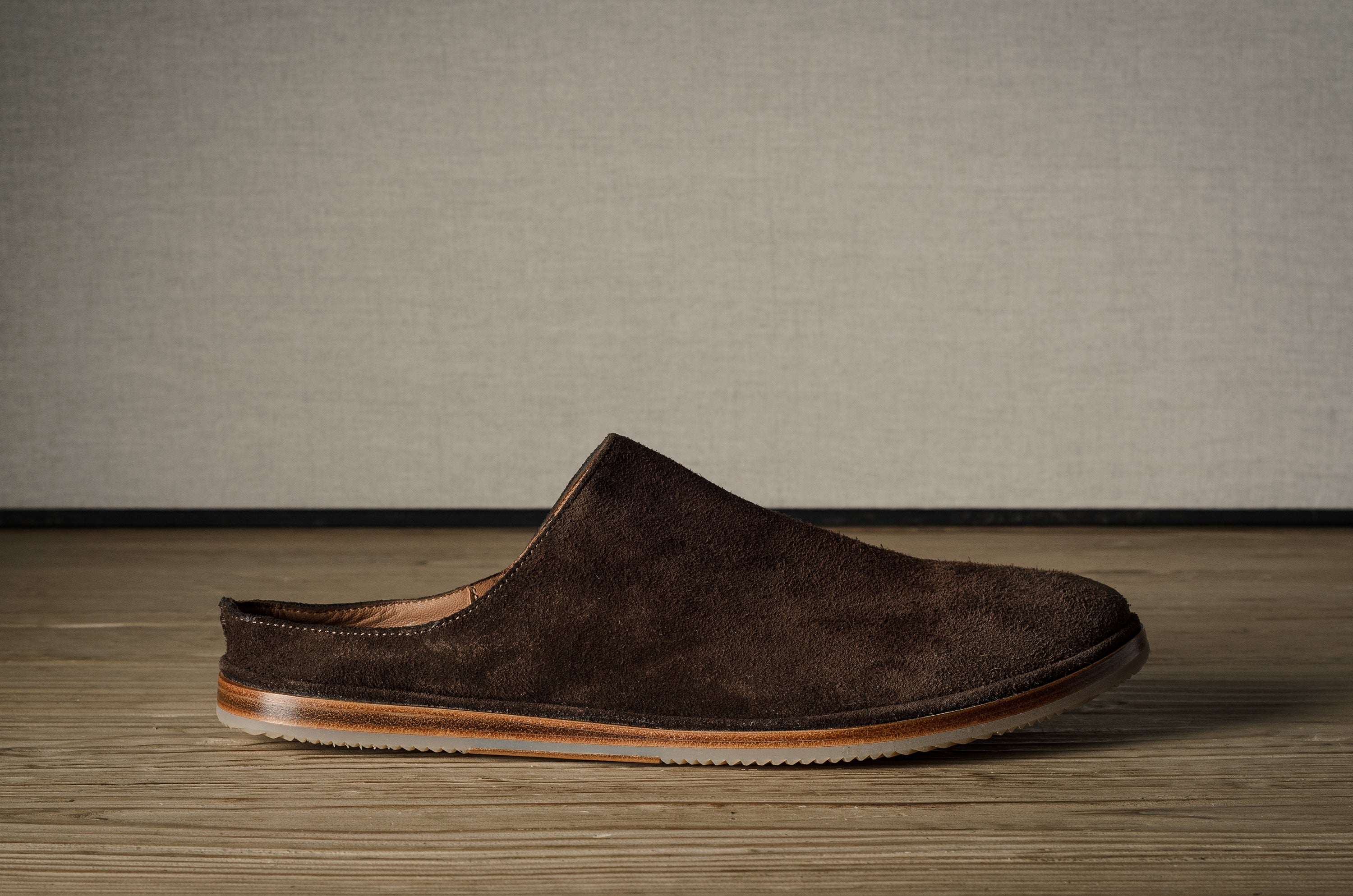 A Brown suede slipper on a wooden background.