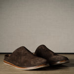 Pair of brown suede slippers on a wooden background.