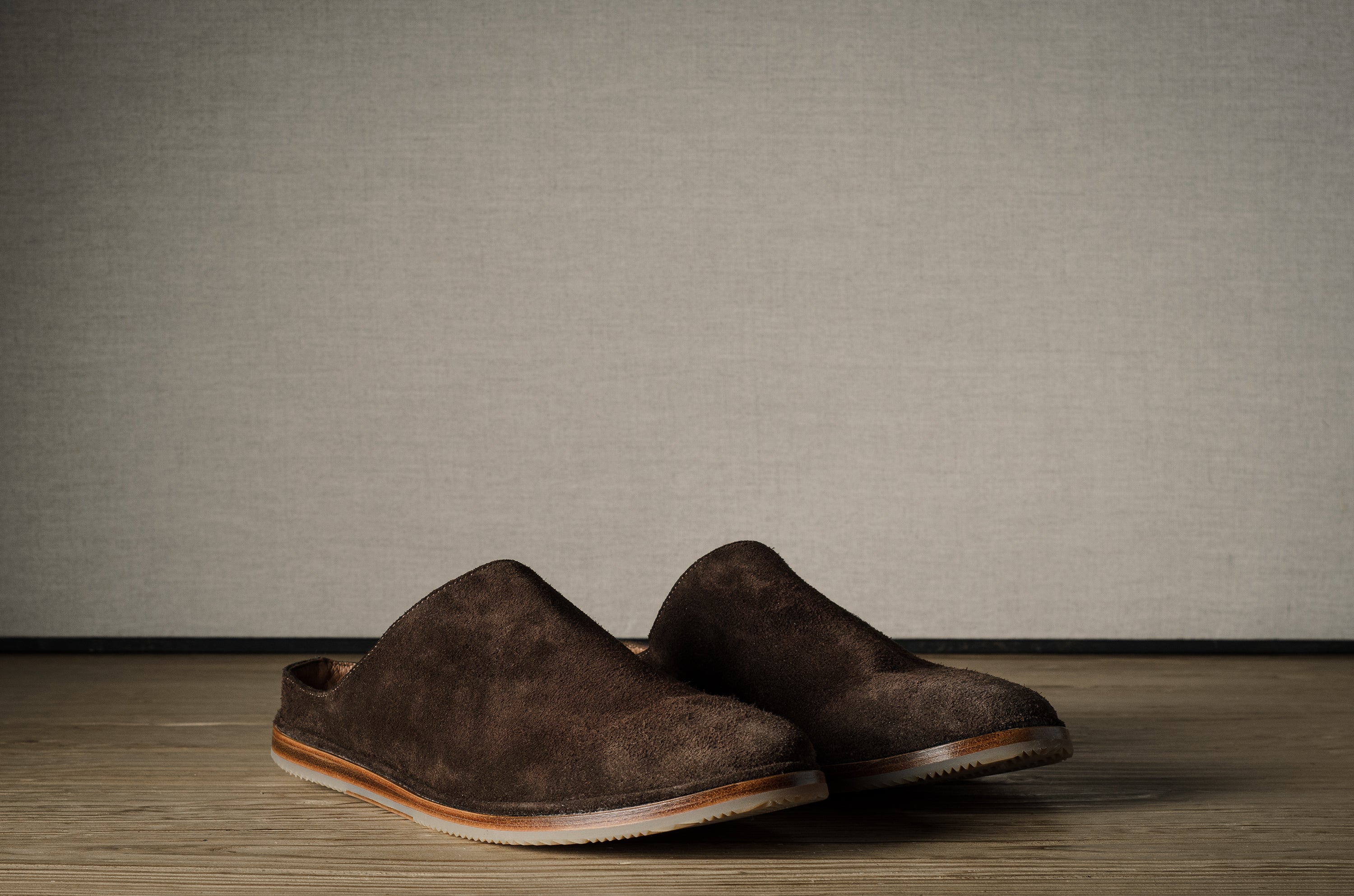 Pair of brown suede slippers on a wooden background.