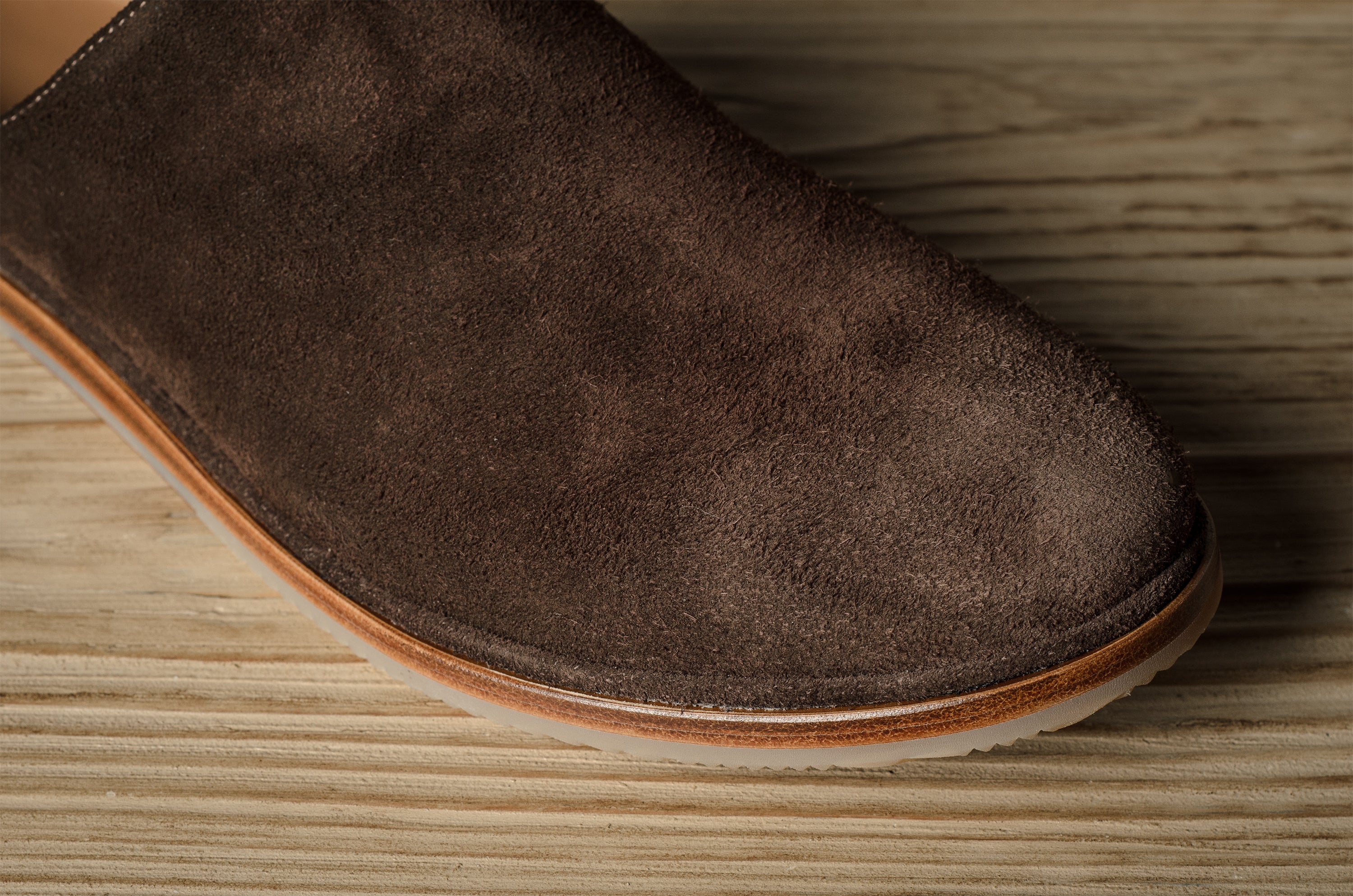 A Brown suede slipper on a wooden background.
