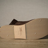 A Brown suede slipper with rubber sole on a wooden background.