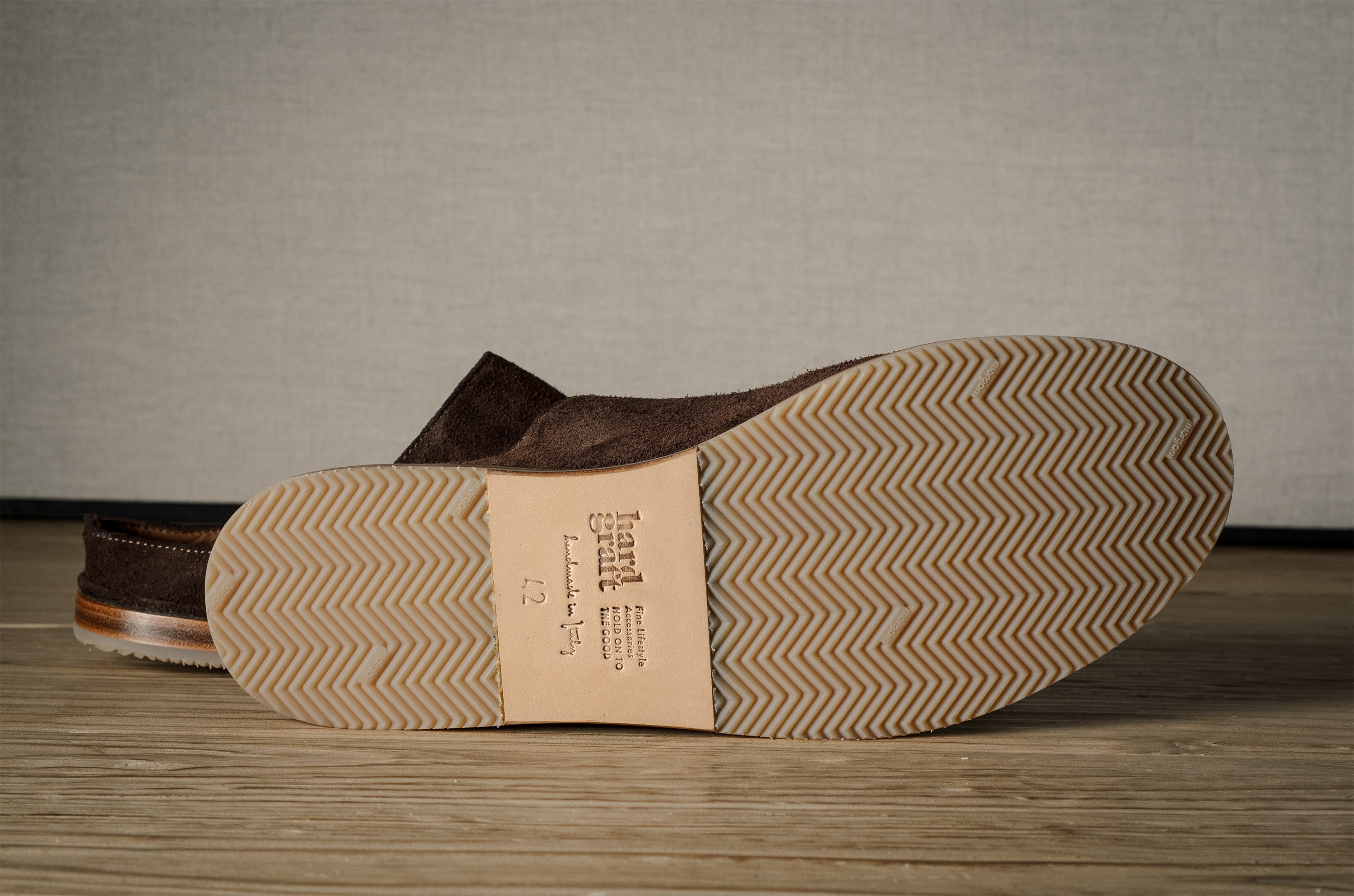 A Brown suede slipper with rubber sole on a wooden background.