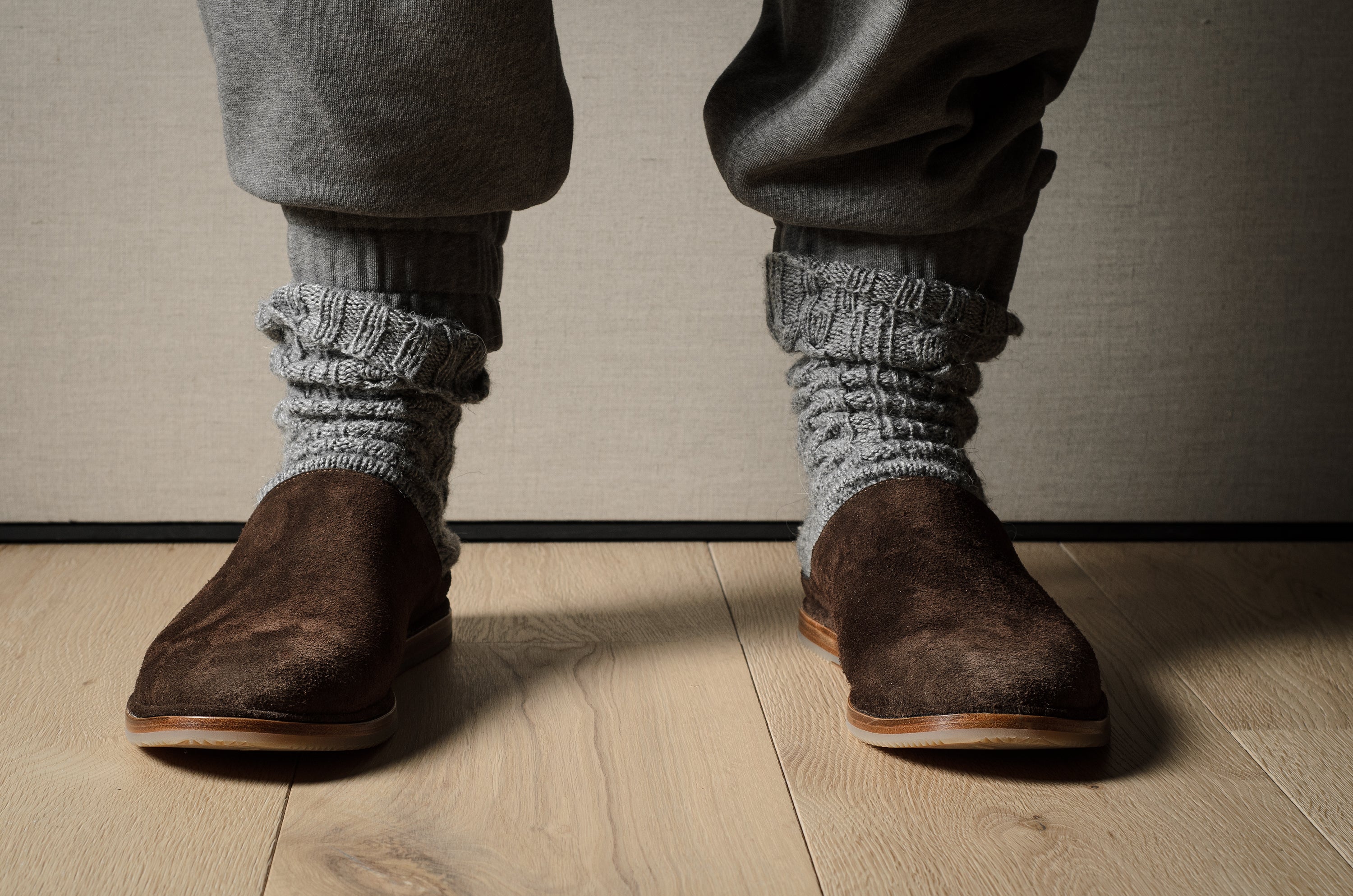 Pair of brown suede slippers on a wooden background.
