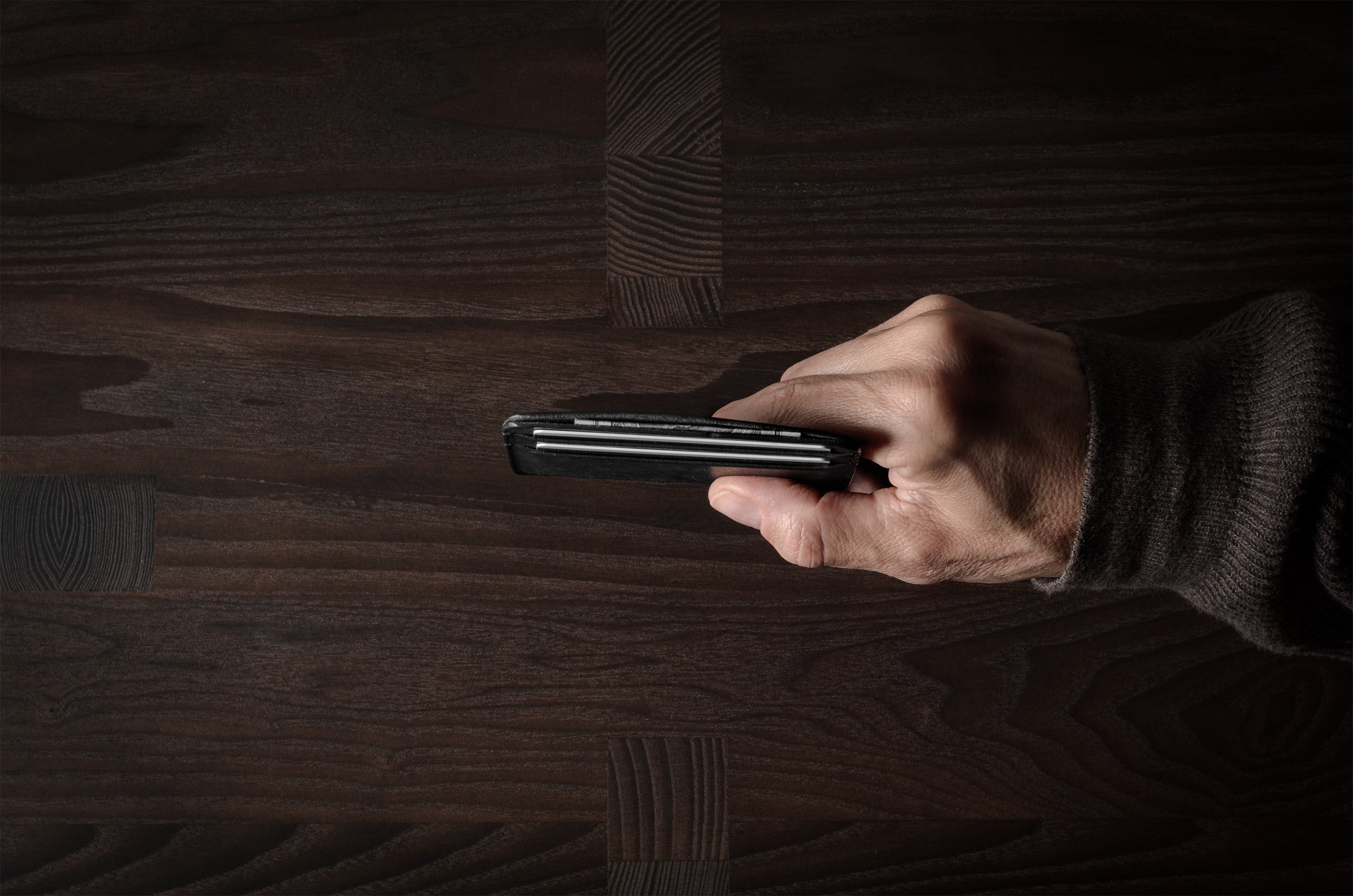 Hand holding a card case on a wooden surface