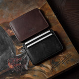 Two card cases on a painted background, one in brown, one in black with cards inside.