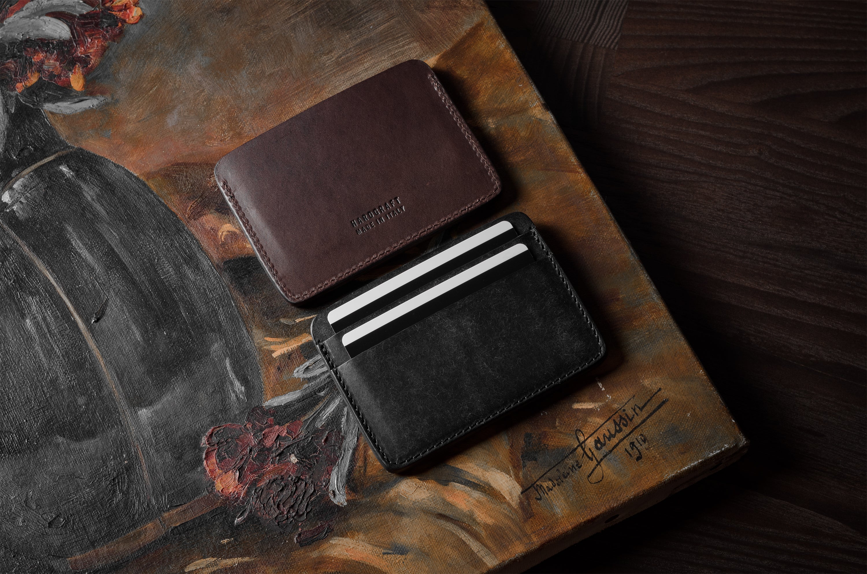 Two card cases on a painted background, one in brown, one in black with cards inside.