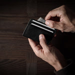 Person holding a black card case with multiple cards on a wooden surface