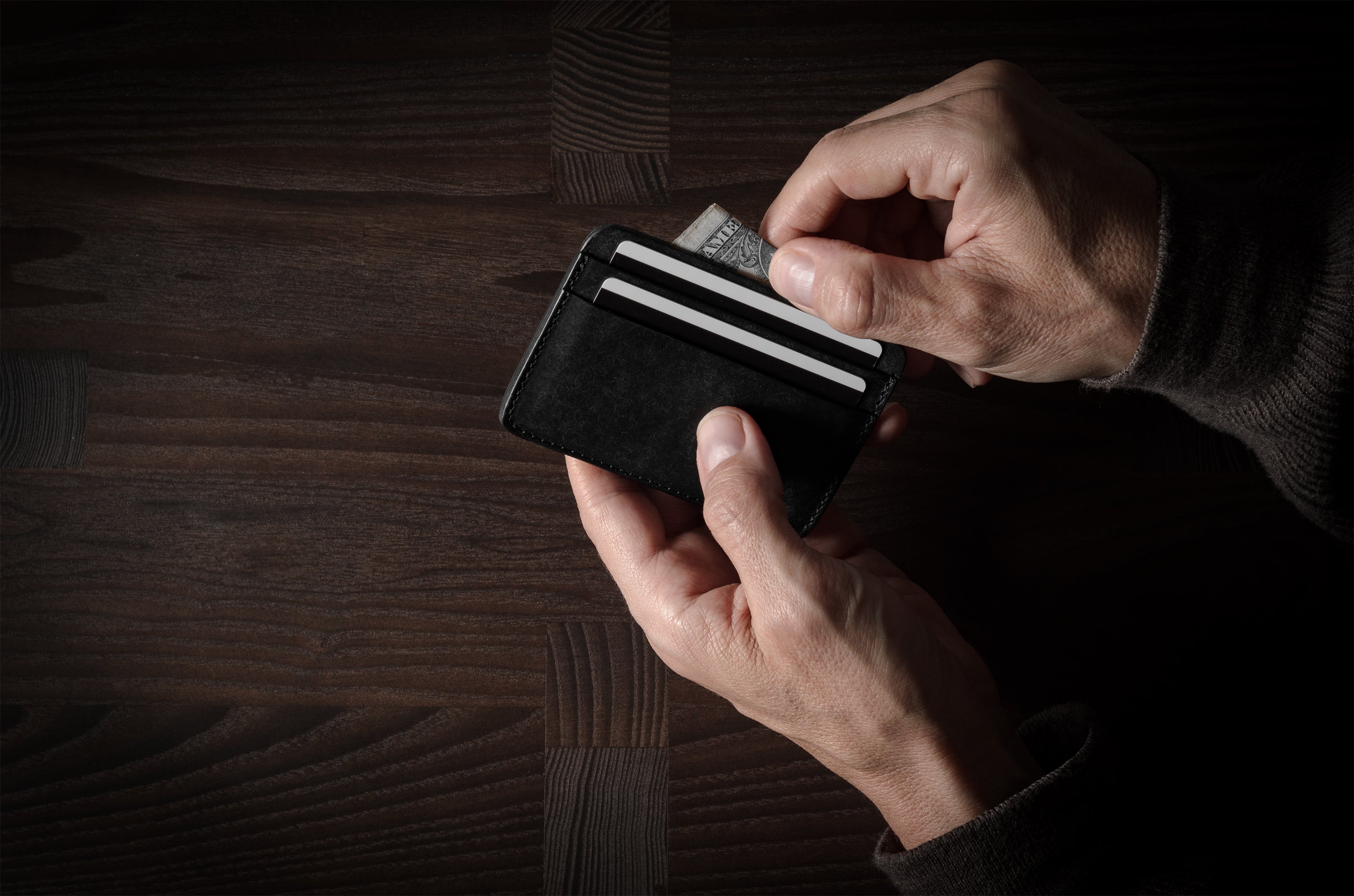 Person holding a black card case with multiple cards on a wooden surface