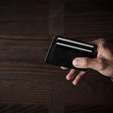 Hand holding a card case with a credit card on a wooden surface