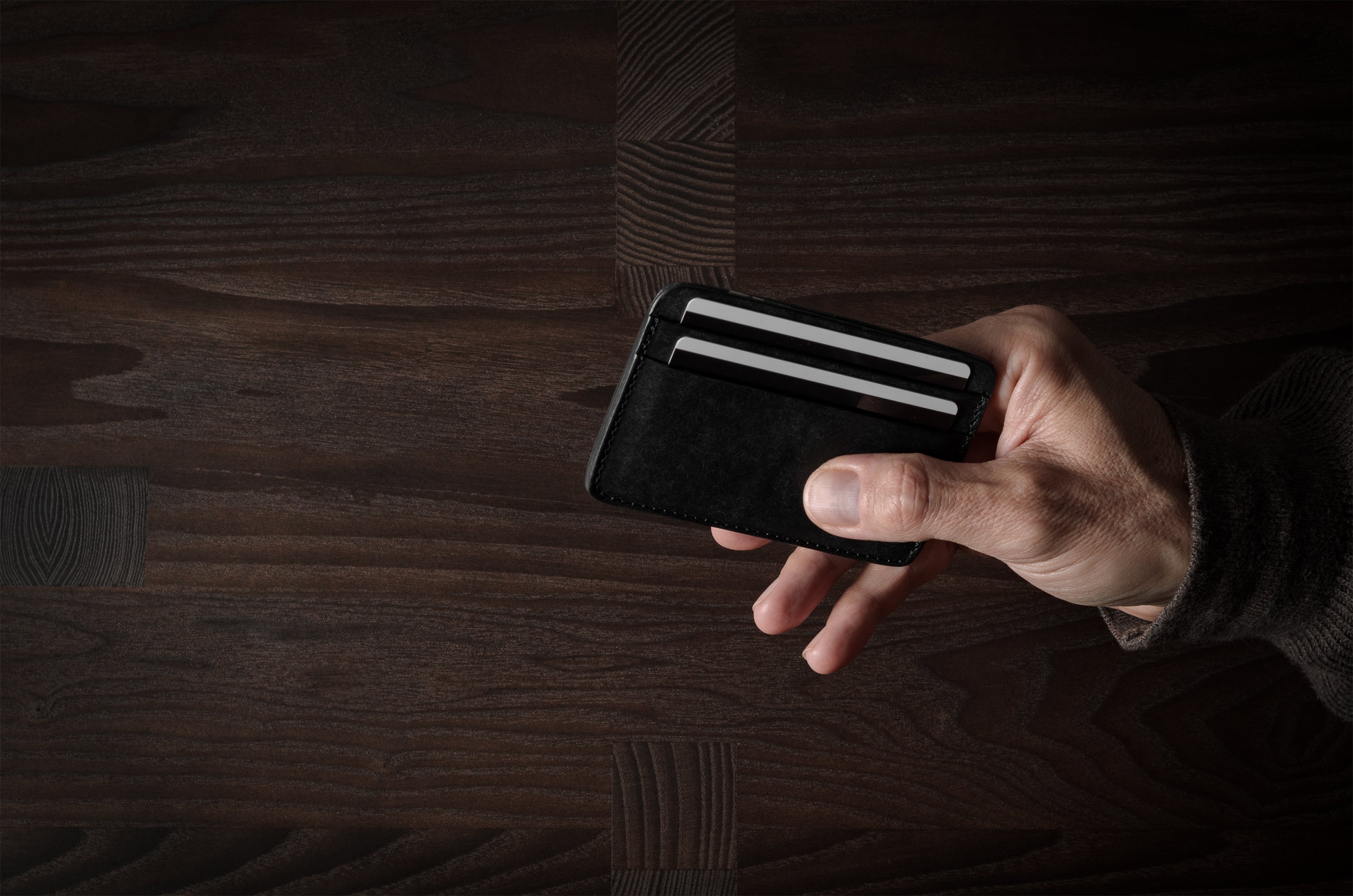 Hand holding a card case with a credit card on a wooden surface