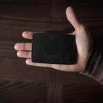 Hand holding a black leather card case on a wooden surface