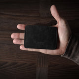 Hand holding a black leather card case on a wooden surface