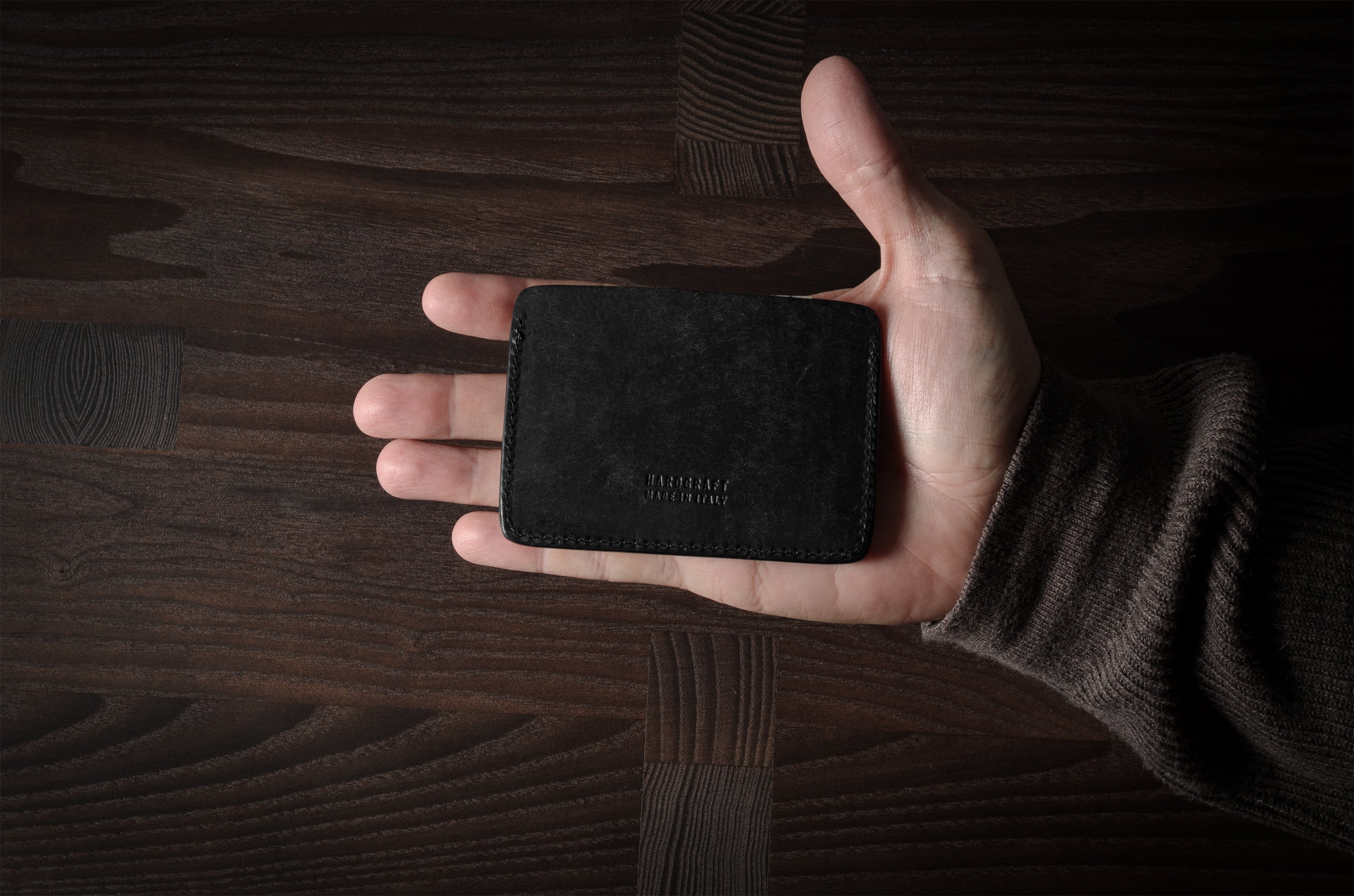 Hand holding a black leather card case on a wooden surface