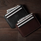 Two card cases on a dark wood background, one in brown, one in black with cards inside.