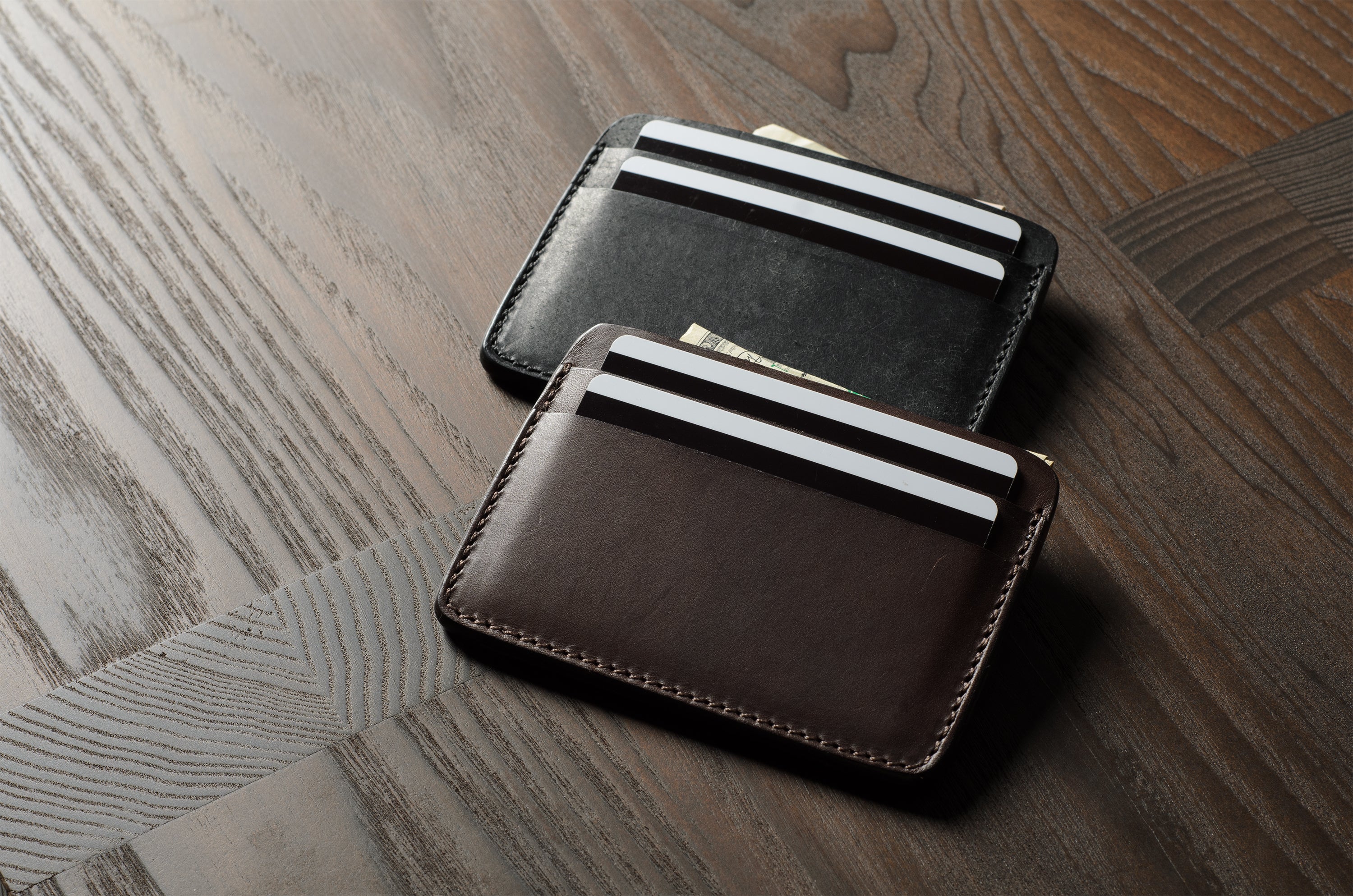 Two card cases on a dark wood background, one in brown, one in black with cards inside.