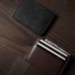 Two card cases on a dark wood background, one in brown, one in black with cards inside.