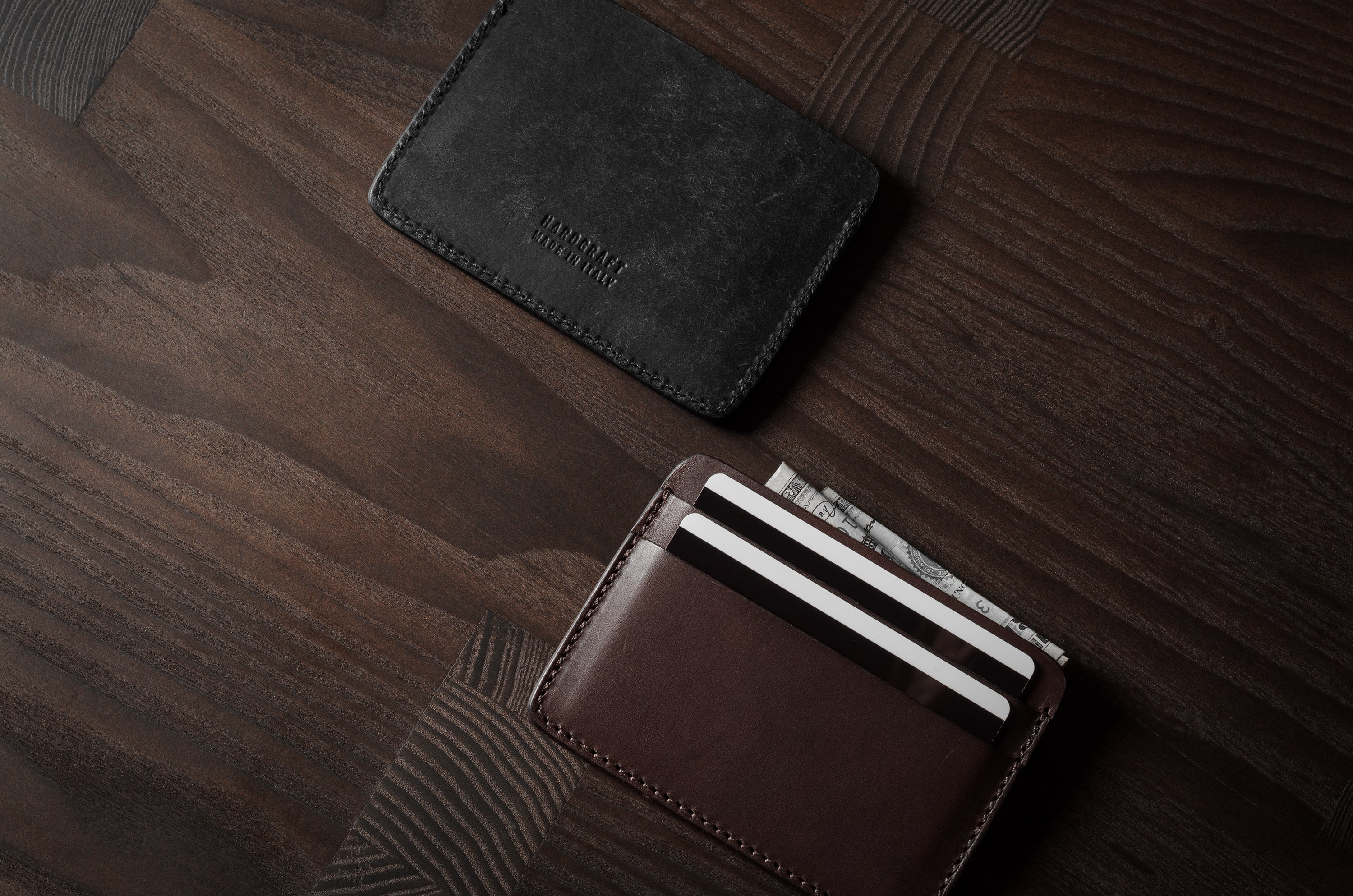 Two card cases on a dark wood background, one in brown, one in black with cards inside.