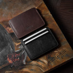 Two card cases on a painted background, one in brown, one in black with cards inside.