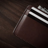 Brown leather card case with cards inside on a dark wood background.