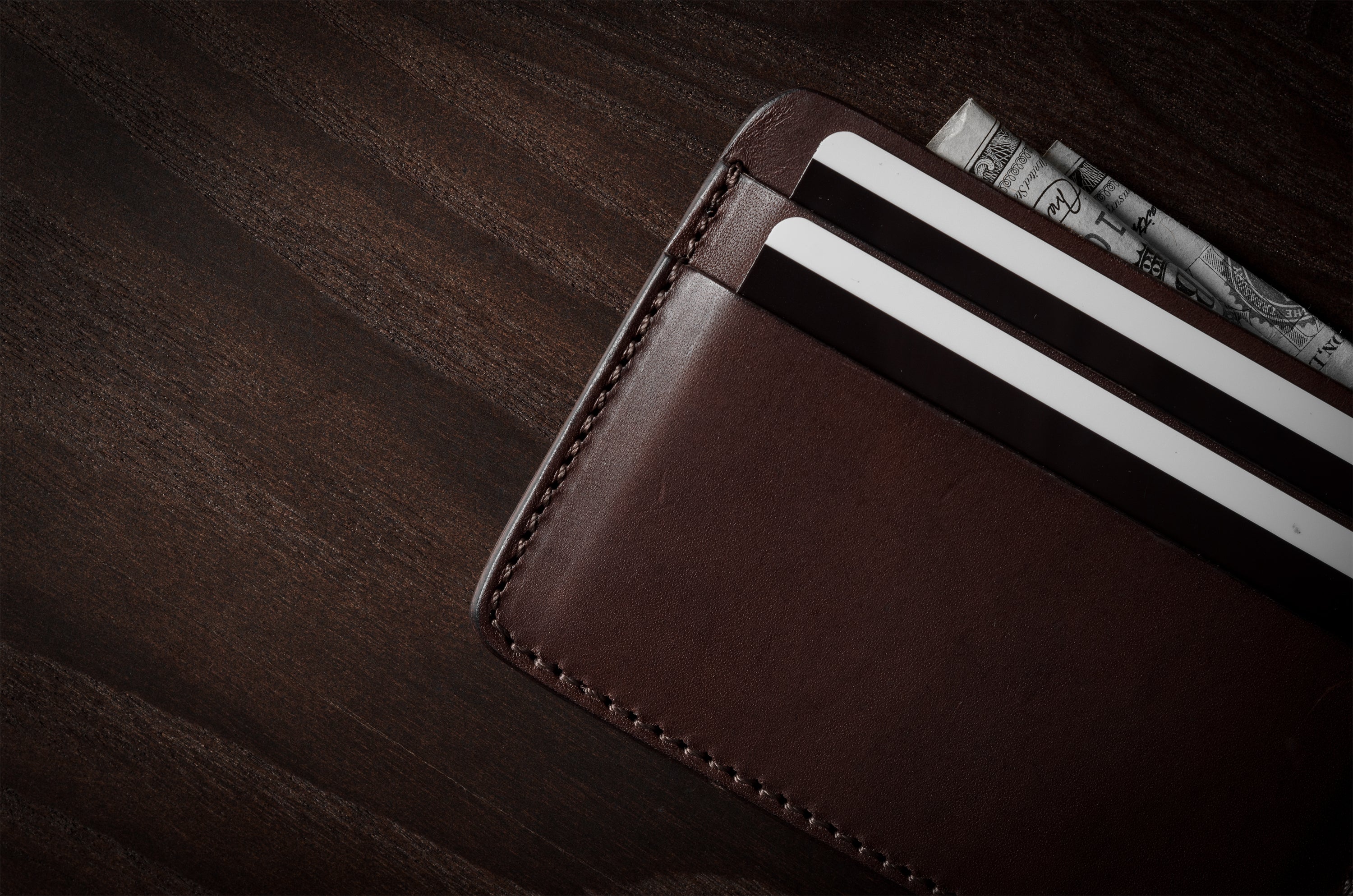 Brown leather card case with cards inside on a dark wood background.