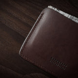 Brown leather card case with cash inside on a dark wood background.
