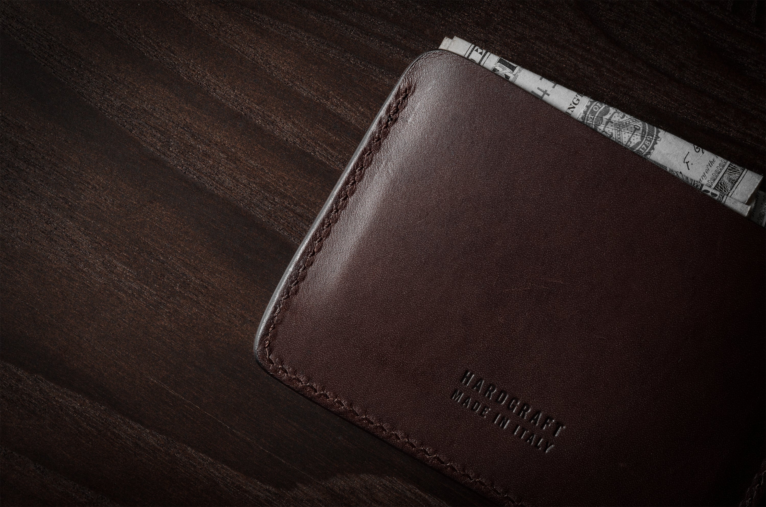 Brown leather card case with cash inside on a dark wood background.