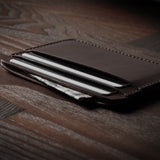 Brown leather card case with cards inside on a dark wood background.