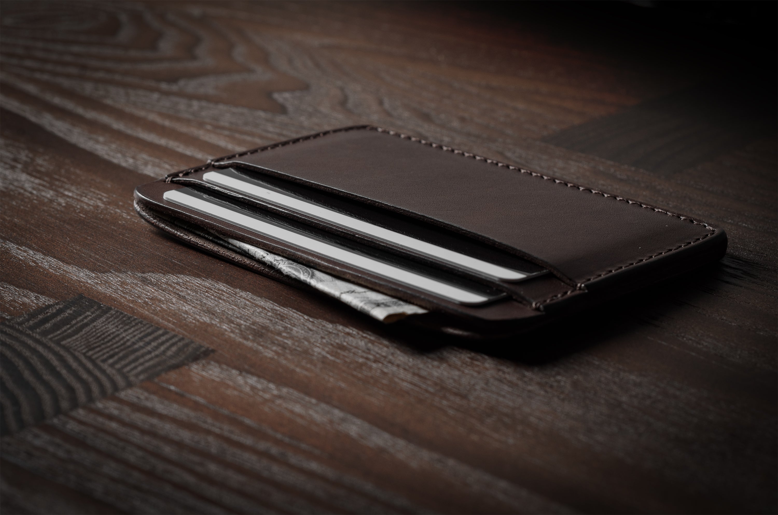 Brown leather card case with cards inside on a dark wood background.