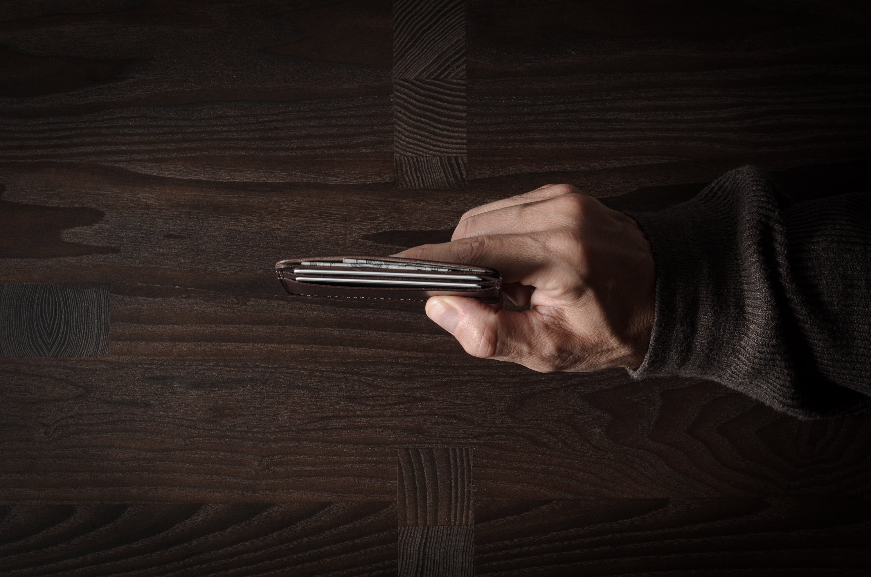 Brown leather card case with cards inside on a dark wood background.