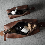 Two brown leather zippered pouches arranged on a gray textured surface, each open to show toiletry items inside.