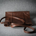 A brown leather tote bag with a matching shoulder strap, displayed on a textured gray background.