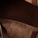 Close-up of a brown leather and suede tote bag interior, showing stitched panels and a small debossed brand mark reading Made in Italy.