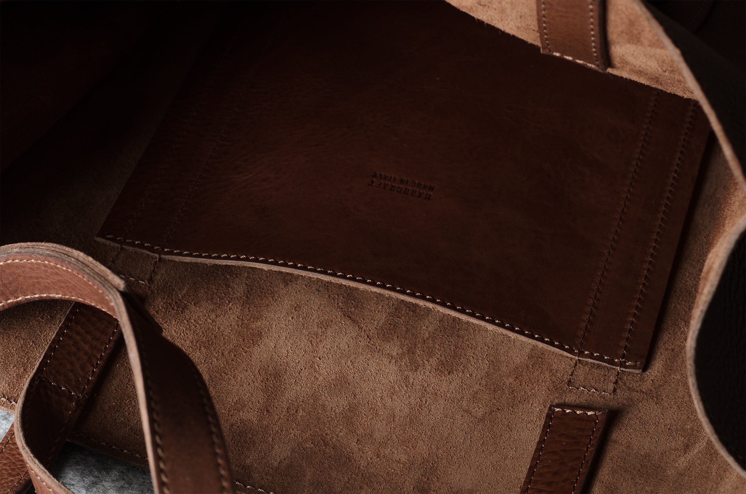 Close-up of a brown leather and suede tote bag interior, showing stitched panels and a small debossed brand mark reading Made in Italy.
