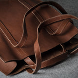 A close-up of a brown pebbled leather tote bag with matching leather handles, resting on a textured gray surface.