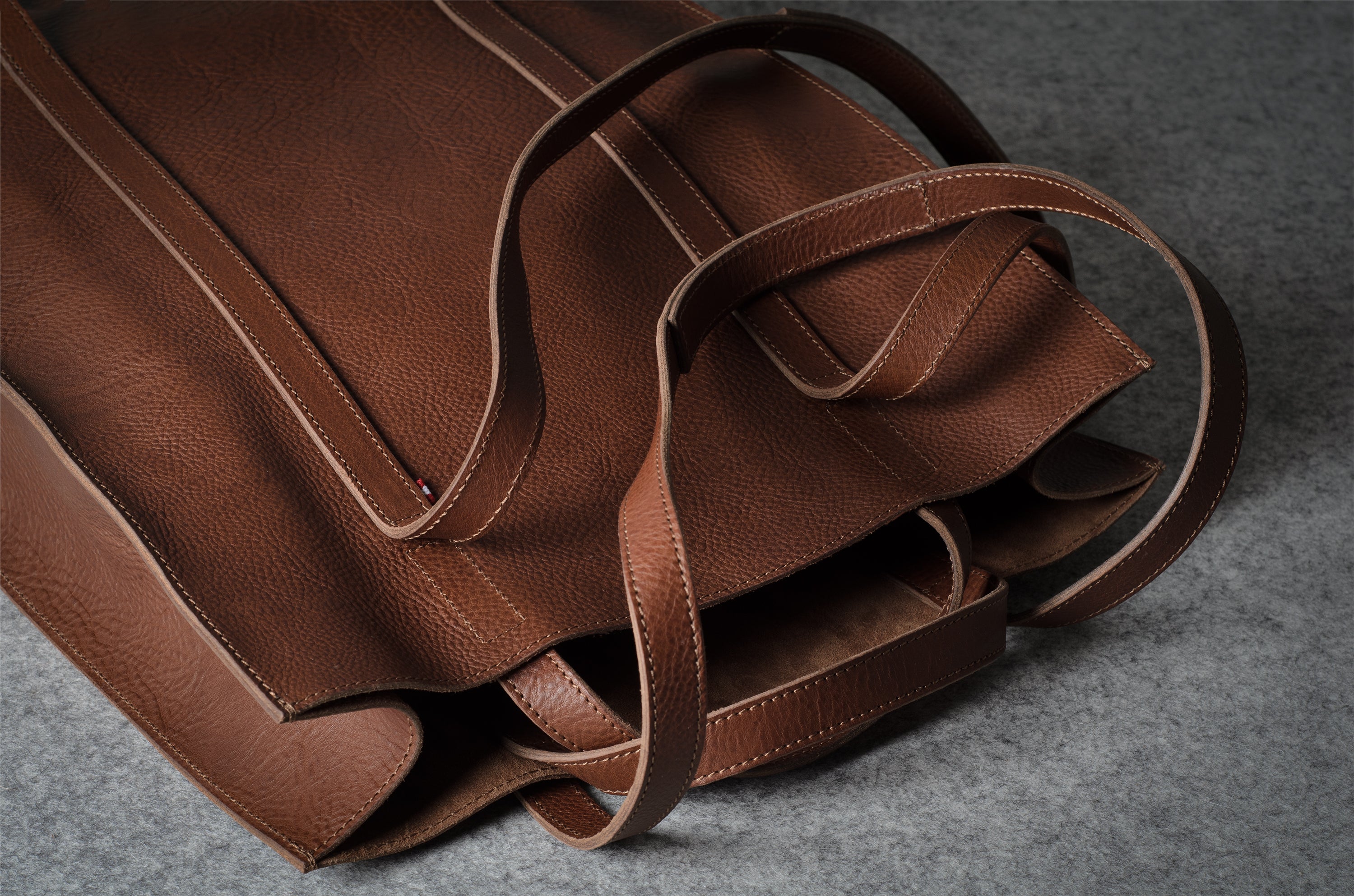A close-up of a brown pebbled leather tote bag with matching leather handles, resting on a textured gray surface.