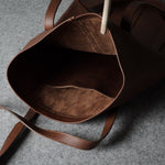 A close-up of a dark brown leather tote bag shown from the inside, highlighting the rich brown interior lining and matching shoulder straps on a textured gray surface.