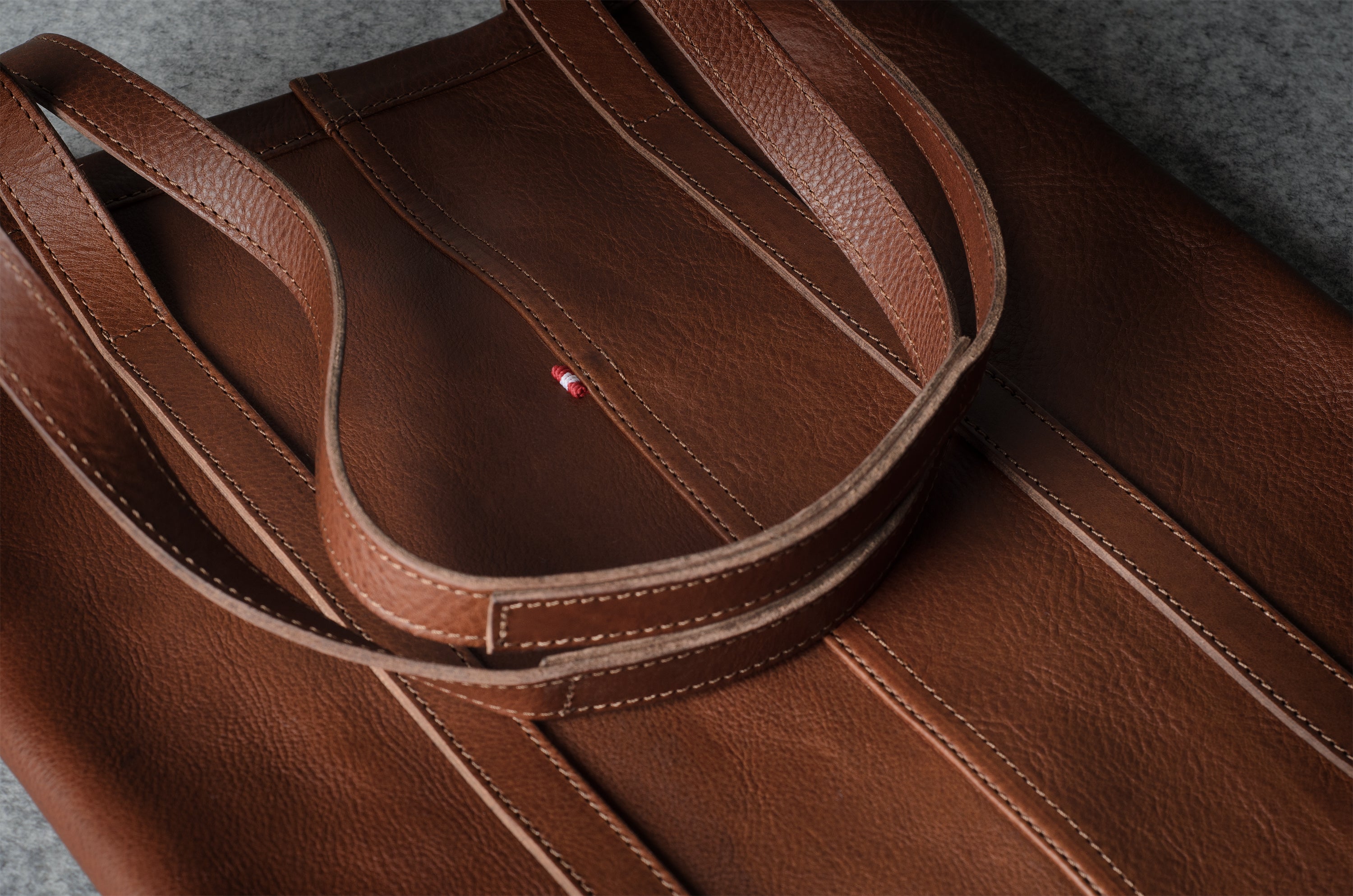 Close-up of a brown leather tote bag with matching shoulder straps, showing fine stitching and a small red brand tab.