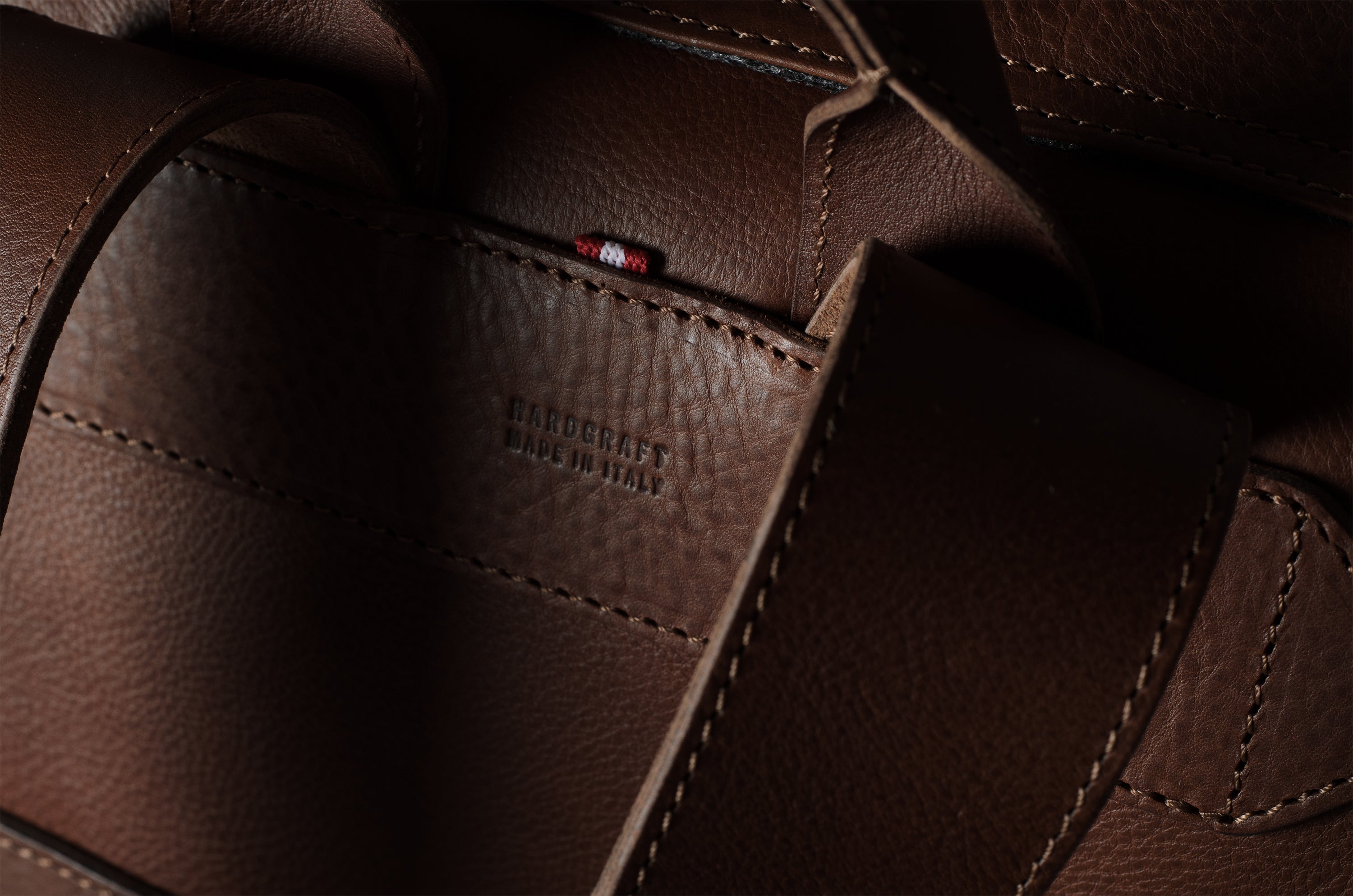 Close-up of a dark brown leather bag showing the interior lining, stitching, and a small red brand tab with white text reading ‘HARDGRAFT MADE IN ITALY'.