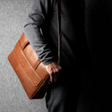 Person holding a brown leather briefcase against a gray background