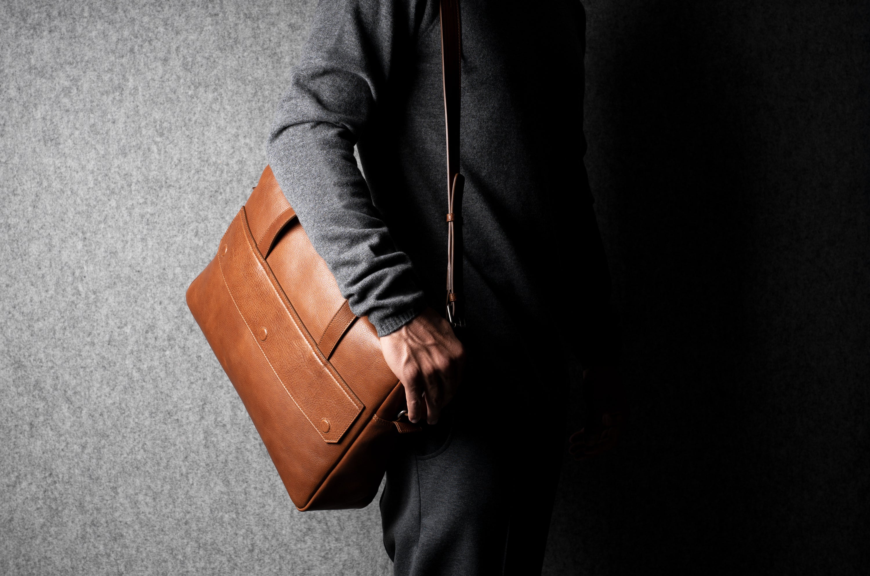 Person holding a brown leather briefcase against a gray background